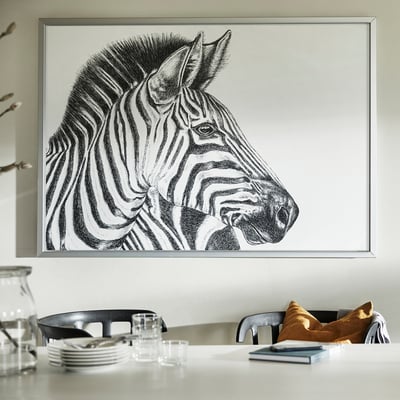 Large framed black and white zebra portrait, BJÖRKSTA, hangs above a white table with chairs and items.