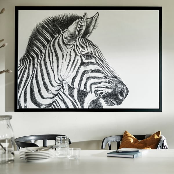 Large zebra portrait framed in black aluminium hangs on a wall over a dining table with chairs.