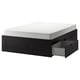 An IKEA BRIMNES black storage bed. It has a rectangular shape with four drawers and a white mattress on top.
