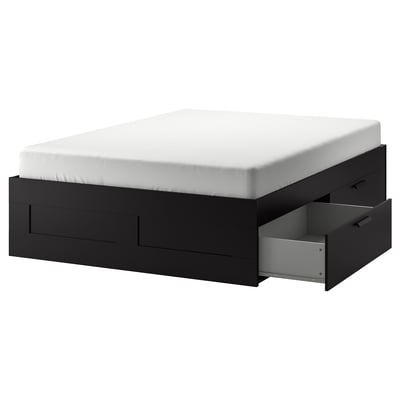 An IKEA BRIMNES black storage bed. It has a rectangular shape with four drawers and a white mattress on top.