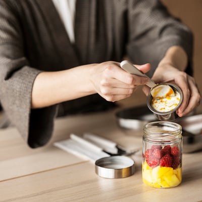 A person makes a fruit and yoghurt parfait in a DAGKLAR jar with a separator on a wooden table among kitchen tools.