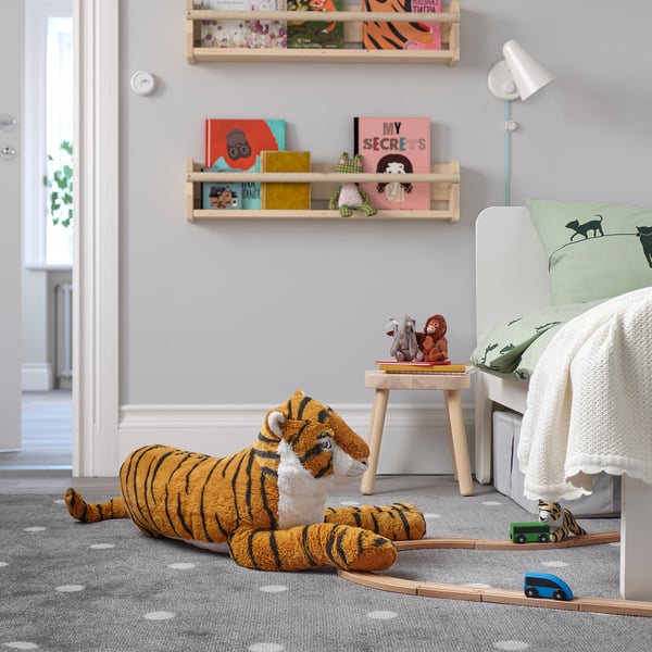Large orangey-brown plush tiger, striped darker, big eyes, soft. Lays next to bed, train cars nearby, shelves with books overhead.