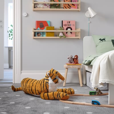 Large orangey-brown plush tiger, striped darker, big eyes, soft. Lays next to bed, train cars nearby, shelves with books overhead.