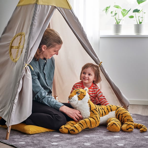 A person and child play in a tent with a large stuffed tiger.