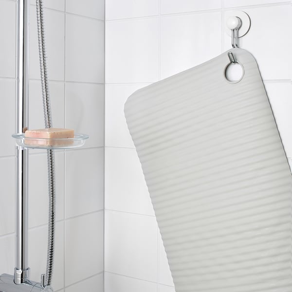 A clear mat hangs in a shower, secured by suction cups, with a bar of soap on a nearby holder.