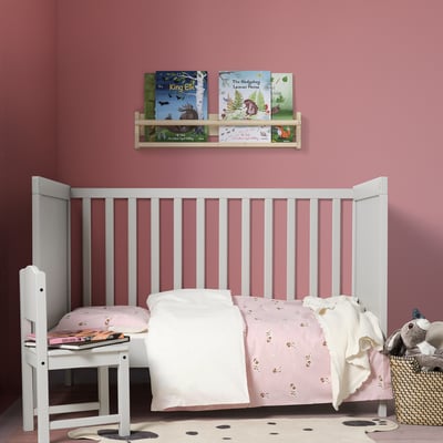 White DRÖMSLOTT kids bed with organic cotton bedding; wooden bookshelf, stuffed animals, pink walls.