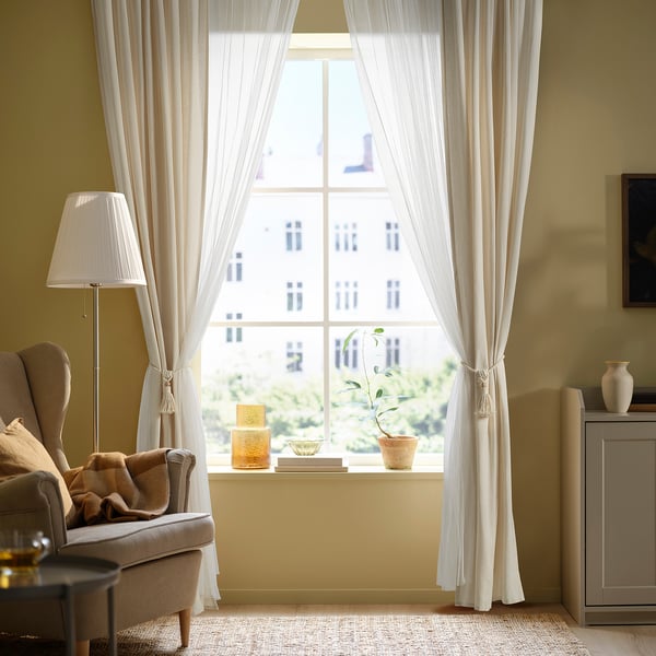 Cosy living room with DUNFLÄTA curtains, armchair, and table decor, yellow walls.