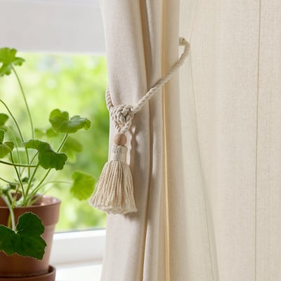 Off-white curtain tie-backs with tassels and beads, held by magnets near a window with a plant.