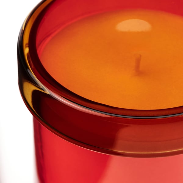 Round, red glass candle jar with orange wax, smooth surface, and a small, centred wick.