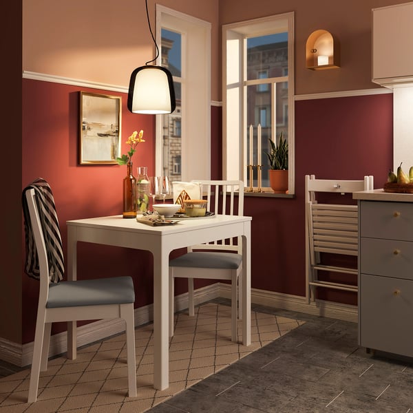Small cosy dining area with white EKEDALEN chairs, grey cushions, marble table, and warm red walls. A hanging lamp illuminates the setup.