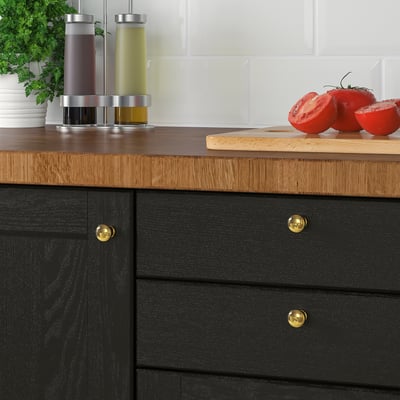 Black kitchen drawer with gold knobs, wooden countertop, fresh tomatoes.