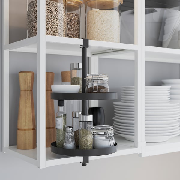 Kitchen cabinet with tiered spice rack, storing jars, bottles, and a grinder.