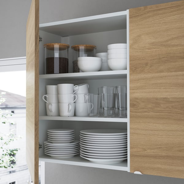 Kitchen cabinet with open shelves, storing white mugs, glasses, bowls, plates, and jars. Organised, accessible, and minimalist design.