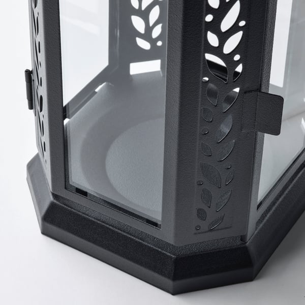Black metal lantern with glass panels, intricate leaf cutouts, robust handle.