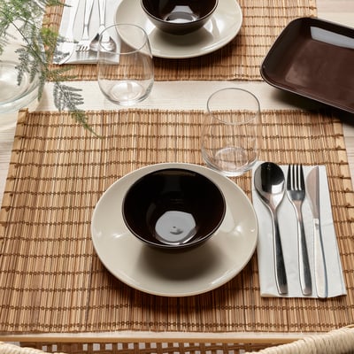 Table setting with beige and black dishes, glasses, cutlery, and a woven placemat.