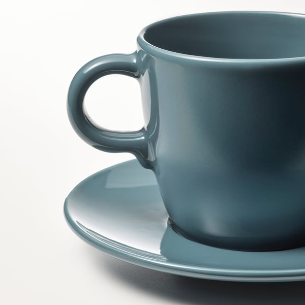 A teal blue mug and matching saucer, made of smooth stoneware, with a glossy finish. The mug has a sturdy handle.