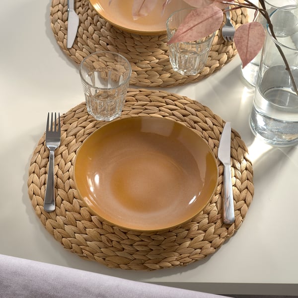 FÄRGKLAR mustard deep plate on woven placemat, larger than glass, with knife/fork, rustic but modern design.