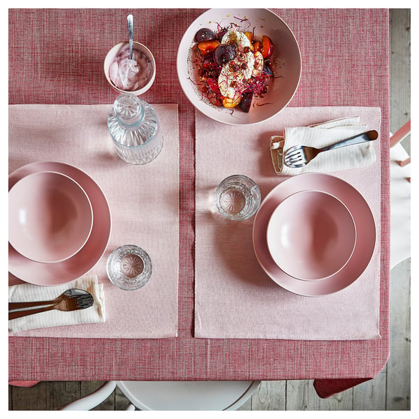 Top view of a table set with pink FÄRGKLAR deep plates, glasses, cutlery, and a bowl of food.