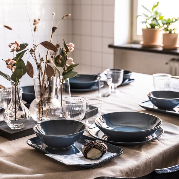 Elegant dining table set with dark blue FÄRGKLAR plates, clear glass vases, and natural floral arrangements.