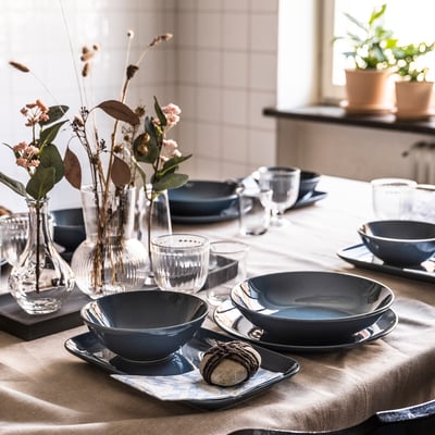 Elegant dining table set with dark blue FÄRGKLAR plates, clear glass vases, and natural floral arrangements.