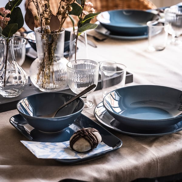 Dinner table with blue stoneware plates, cups, and vases. Simple, elegant design. Floral centrepiece included.