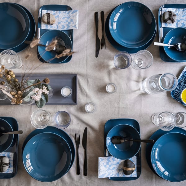 Elegant table setting with blue FÄRGKLAR plates, black cutlery, clear glasses on beige linen.