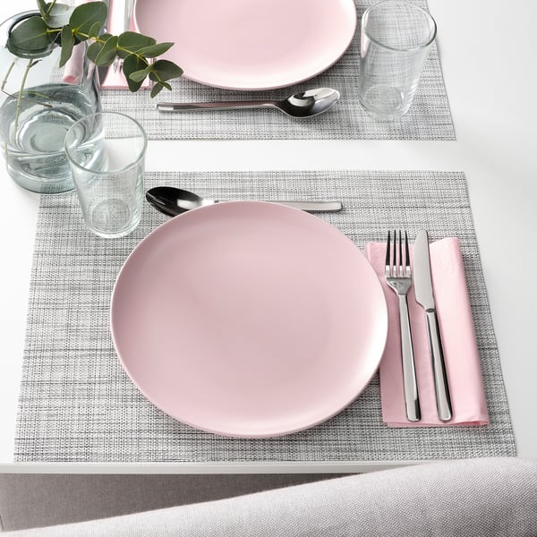 Two place settings with pink plates, silverware, glasses, and napkins on woven placemats.