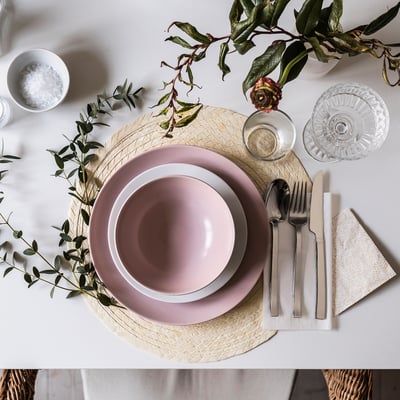 A table set with pink FÄRGKLAR side plates, glassware, silverware, and greenery.