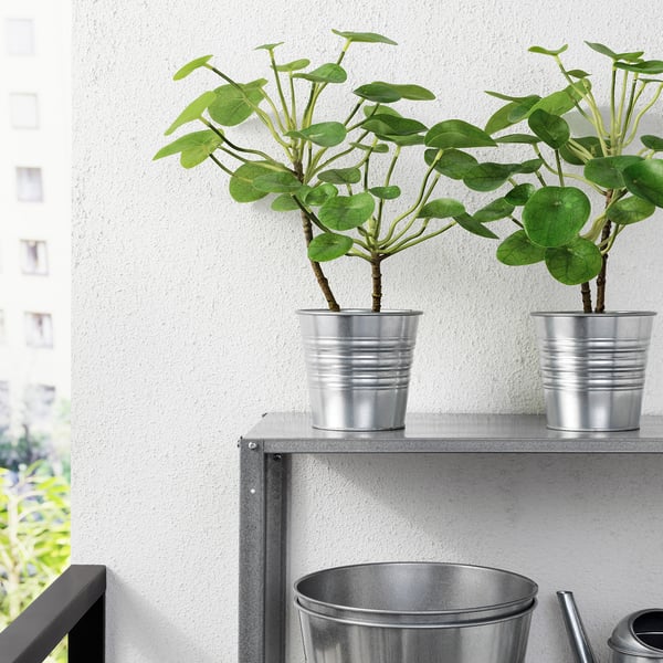 Two potted artificial plants on a metal shelf indoors.