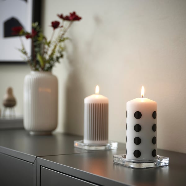 Two lit candles on a table. One is white with black dots, the other has vertical lines. They provide mood lighting and warmth.