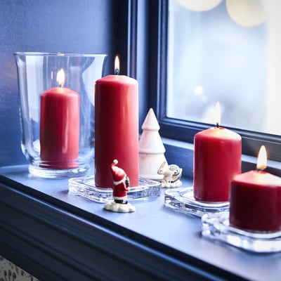 Four lit red candles in clear holders, one small santa figurine, and one small white tree on a dark window sill.