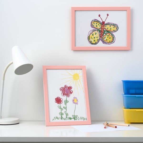 Pink-framed kids art: flowers, butterfly. Lamp, bins nearby.