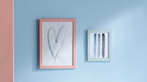 Two framed artworks on blue wall: left - pink heart, right - blue/green strokes.