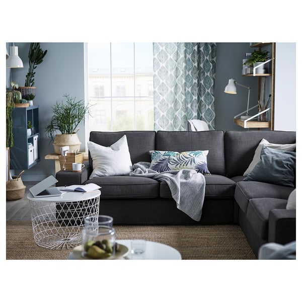 Modern living room with a grey FJÄDERKLINT sofa, white pillows, a coffee table with a laptop, and blue curtains.