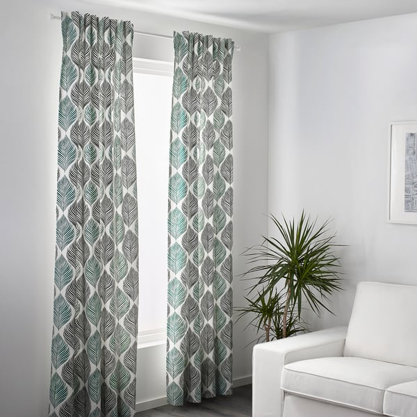Patterned curtains hang by a window, allowing light through, providing privacy, and adorned with a leafy design. A white chair and plant are nearby.