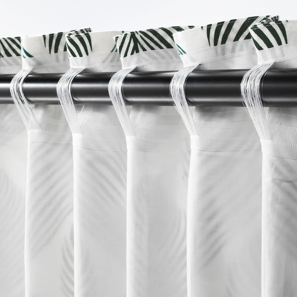 White curtains with leafy pattern top rail hanging on black rod.