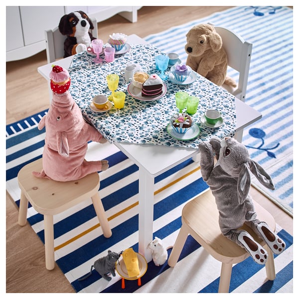 Playful scene: stuffed animals seated at small table with pretzels, tea cups, and plates on a blue-striped rug.