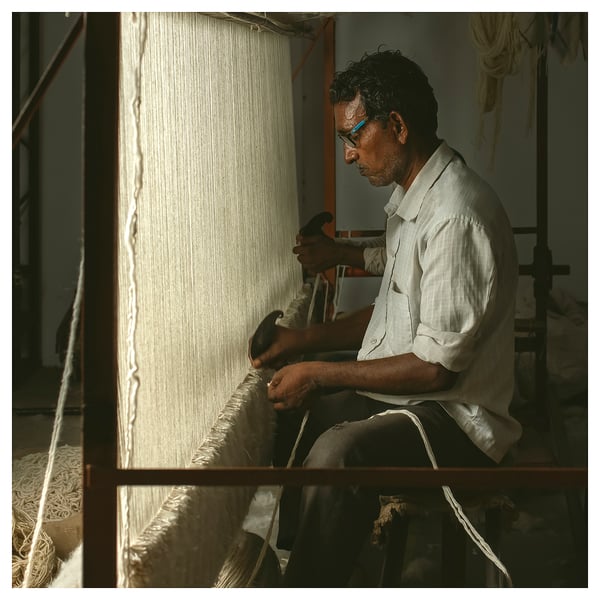 Person weaving fabric on loom, concentrating.