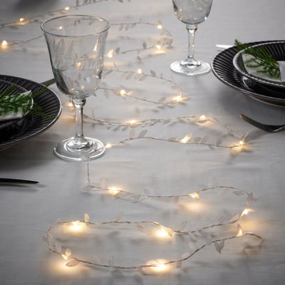 Image a dining table setting with battery-operated leaf-style fairy lights, creating a warm ambiance with wine glasses and plates.