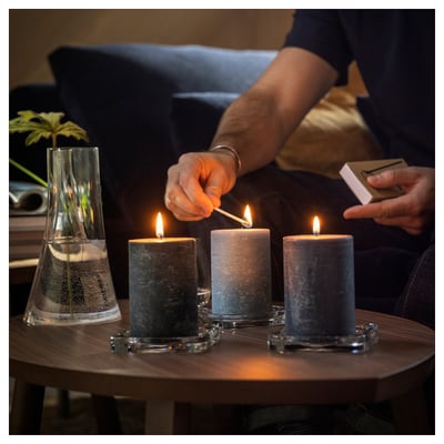 Person lights candles, three grey FRUKTSKOG candles glow on table.