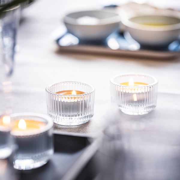 Four small lit candles in clear, ribbed glass holders on a white tablecloth, creating a cosy ambiance.
