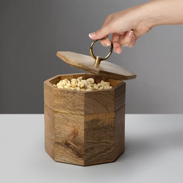 Hand opens wooden snack jar labelled GOKVÄLLÅ, revealing cashews inside. The jar has a lid with a ring for easy access.