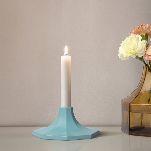 Blue octagon candle holder with lit white candle and nearby vase of pink and yellow flowers.