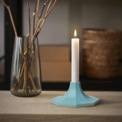 Small blue GOKVÄLLÅ candlestick with lit white candle beside clear vase with branches.