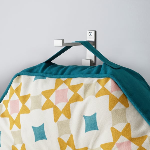 A colourful geometric-patterned floor cushion hangs from a wall hook by its handle.