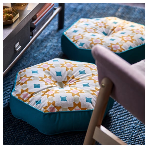 Yellow GOKVÄLLÅ cushions with teal sides on a blue carpet, chair leg visible.