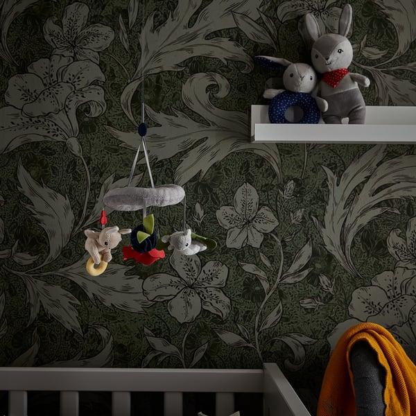 Dark green floral wallpaper, three hanging plush toys and two stuffed animals on shelf.