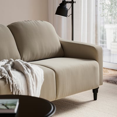 Beige GULLVALLA sofa with black floor lamp, cosy throw, and coffee table.