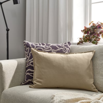 Beige GURLI throw pillow on cushioned chair, medium size, next to dark patterned pillow.