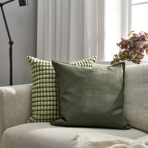 A cosy living room with an olive green GURLI cushion on a light sofa, enhancing decor with textured design and soft fabric.
